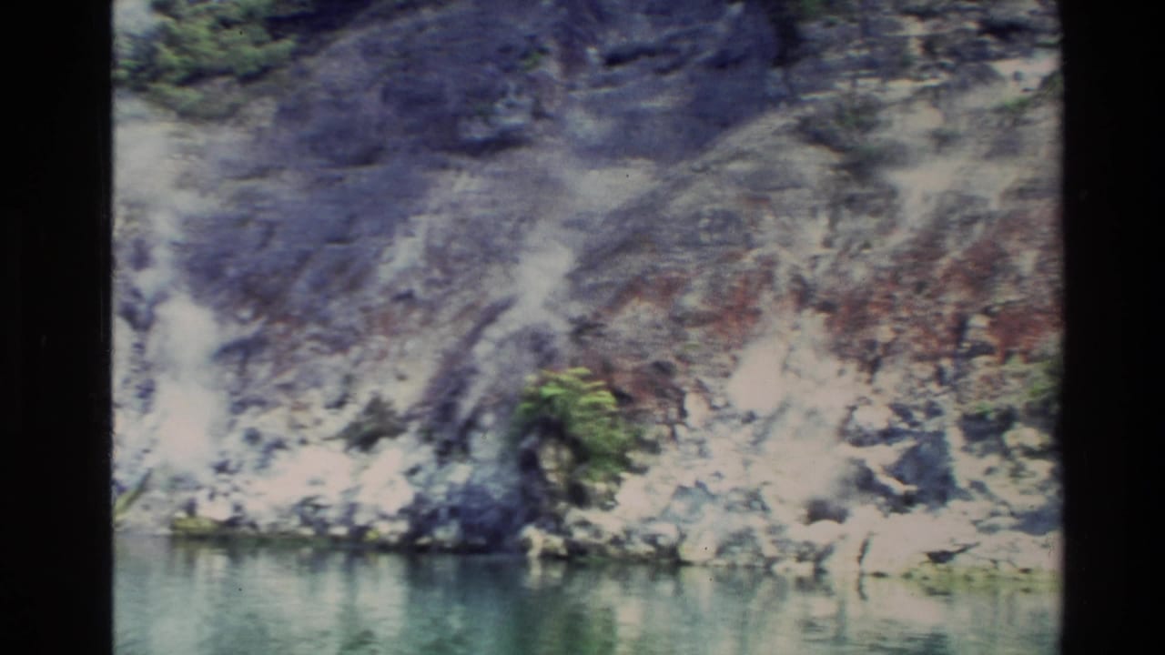 1981 New Zealand 8mm travel frame showing a rocky, mossy cliff reflected near a calm river edge.