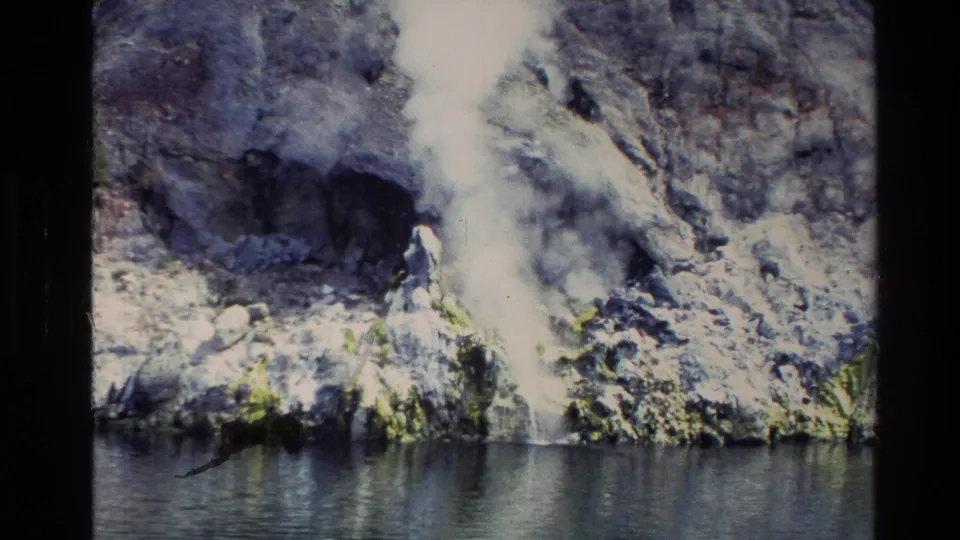 1981 New Zealand 8mm frame with a small waterfall dropping through a rocky, mossy cliff into the river.