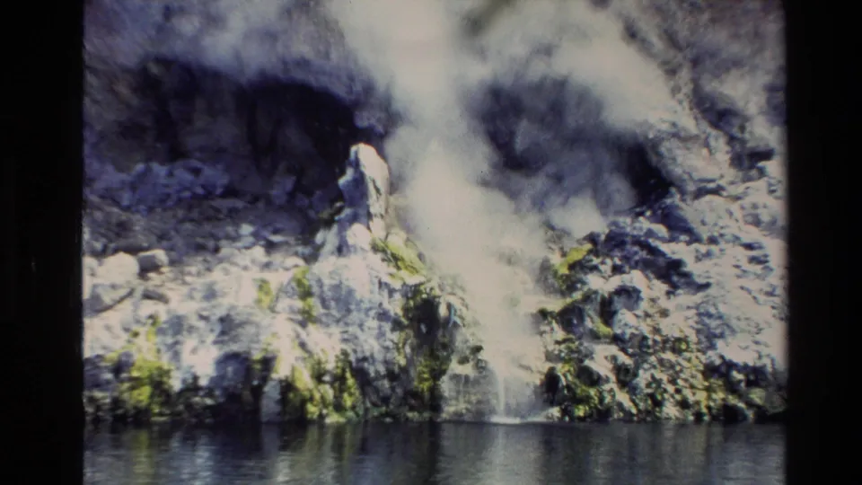 1981 New Zealand 8mm frame showing waterfall spray against a dark rocky cliff near the river.