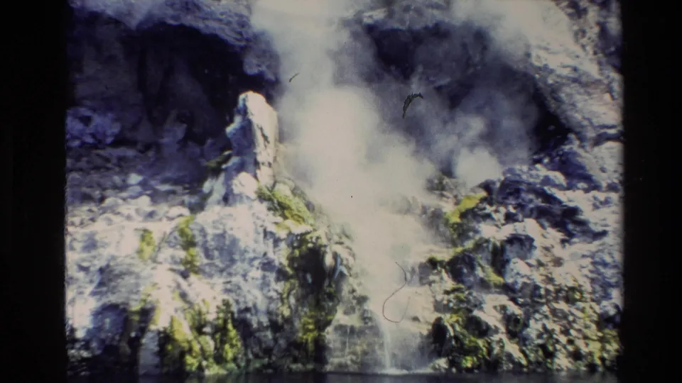 1981 New Zealand 8mm travel frame showing a close view of steam rising from rocky geothermal ground beside calm water.