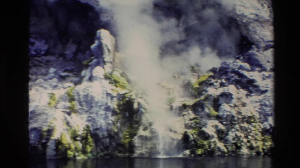 Close 8mm frame of steam drifting over rocks along a New Zealand shoreline, with water at the bottom of the view.