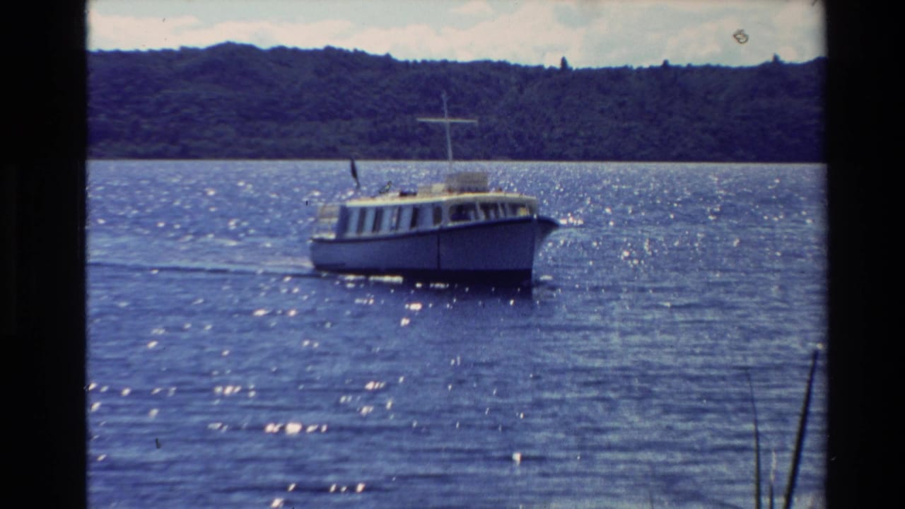 1981 New Zealand 8mm frame showing a small white motorboat on sparkling blue water with a forested shoreline in the distance.