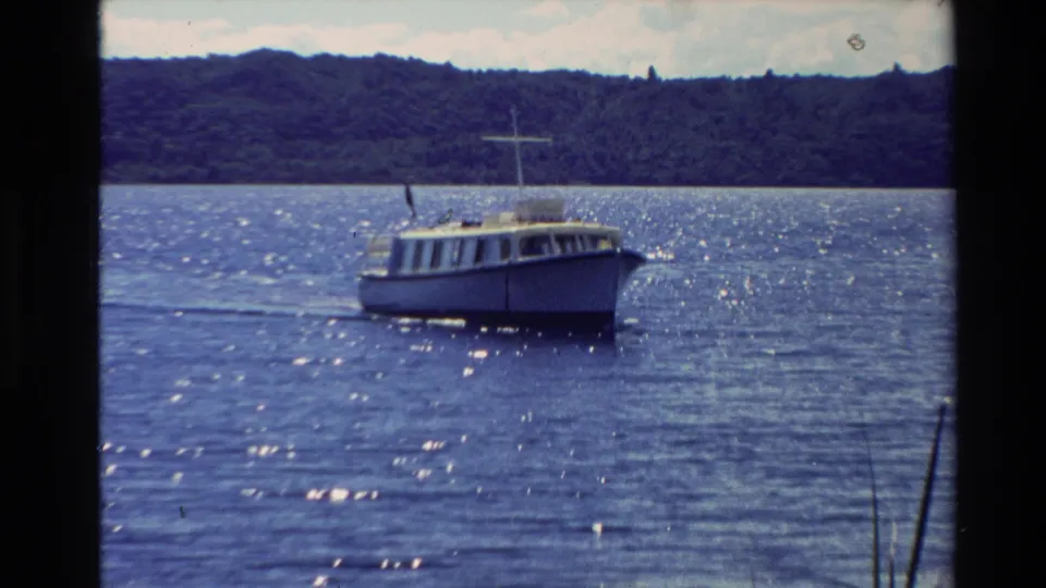 1981 New Zealand 8mm frame showing a small white motorboat on sparkling blue water with a forested shoreline in the distance.