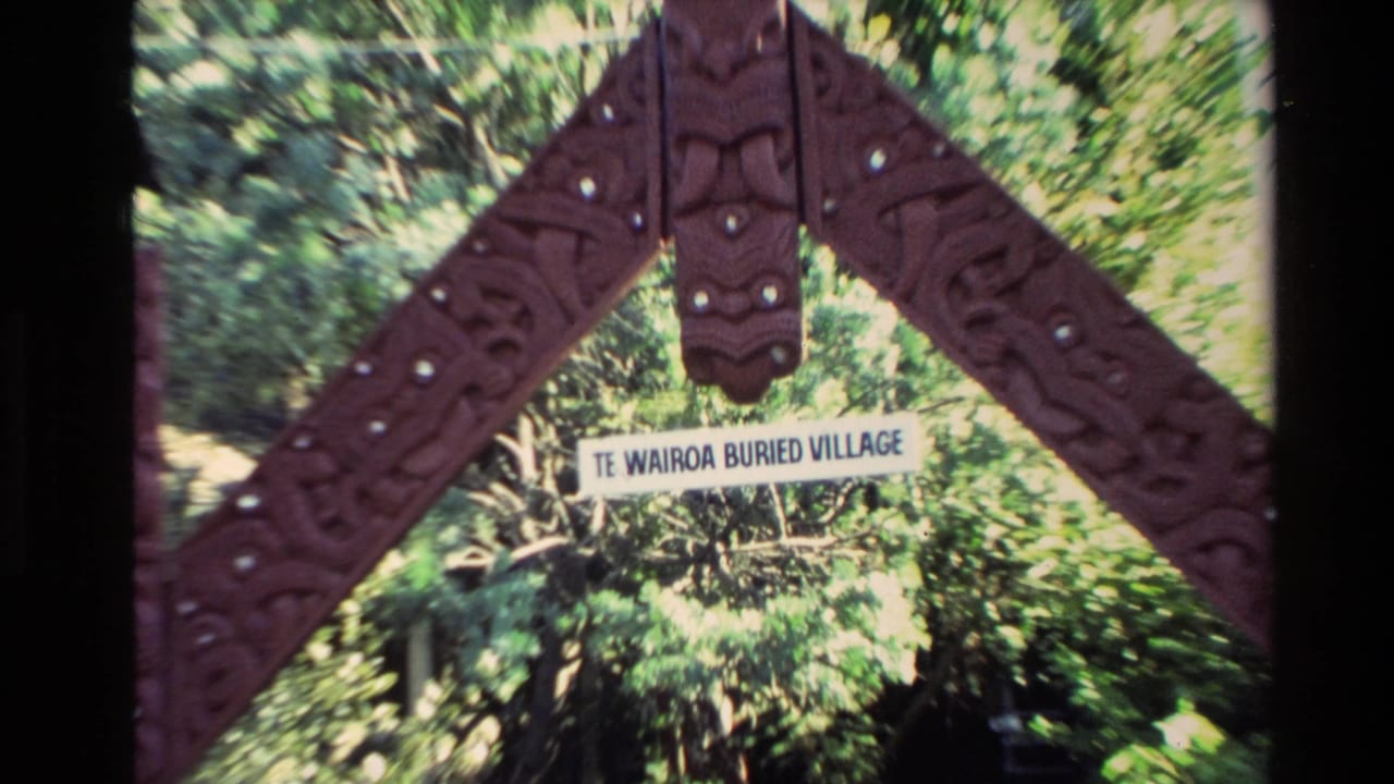 1981 New Zealand 8mm frame showing a carved wooden entrance arch and Te Wairoa Buried Village sign surrounded by greenery.