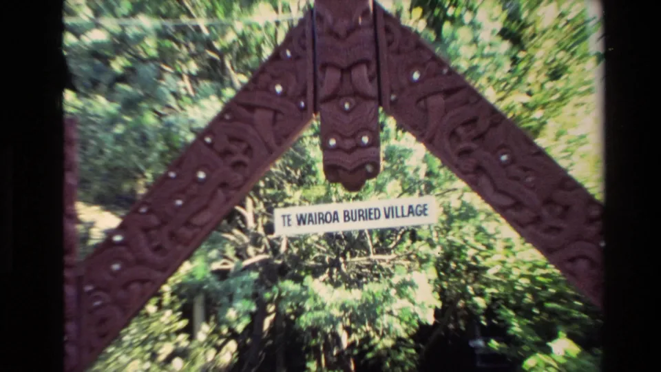1981 New Zealand 8mm frame showing a carved wooden entrance arch and Te Wairoa Buried Village sign surrounded by greenery.