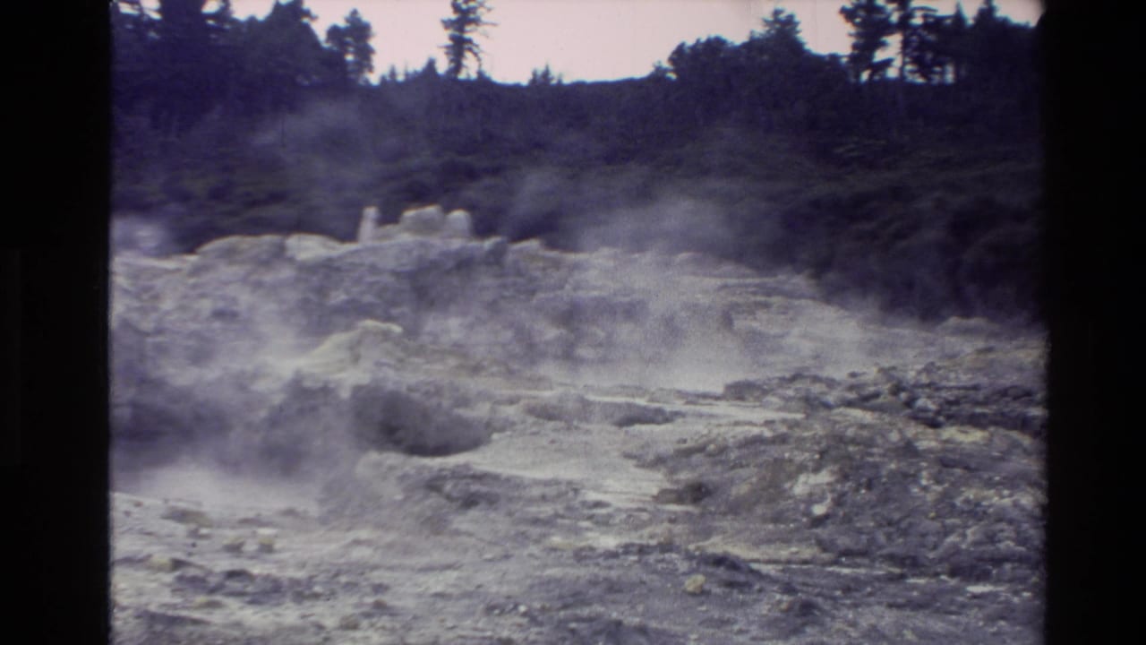 New Zealand 1981 8mm frame showing steam rising from mineral-stained rocky terrain with distant trees and dark film borders.