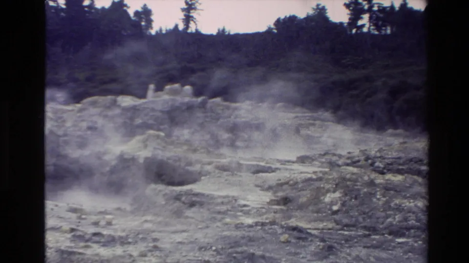 New Zealand 1981 8mm frame showing steam rising from mineral-stained rocky terrain with distant trees and dark film borders.