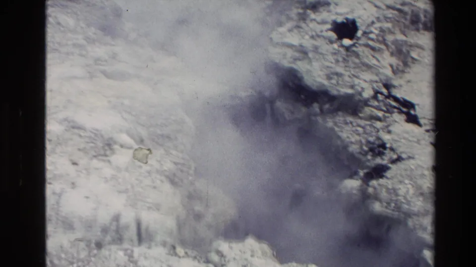 Close 1981 New Zealand 8mm view of a geothermal vent or crevasse releasing steam over pale, rough mineral deposits.