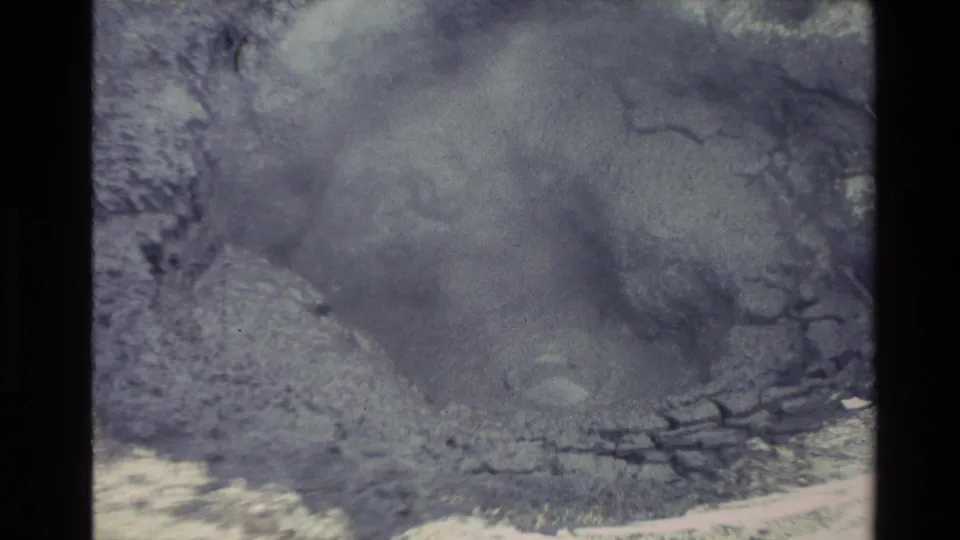Close 1981 New Zealand 8mm view of a bubbling geothermal mud pit, with steam softening the rocky edges and pale mineral surface.