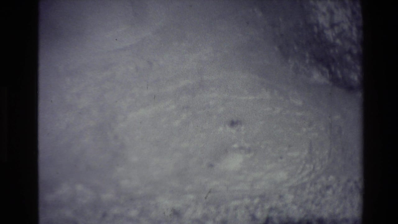 Faded 8mm frame from the New Zealand geothermal clip showing an indistinct dark surface with pale steam or mineral haze.