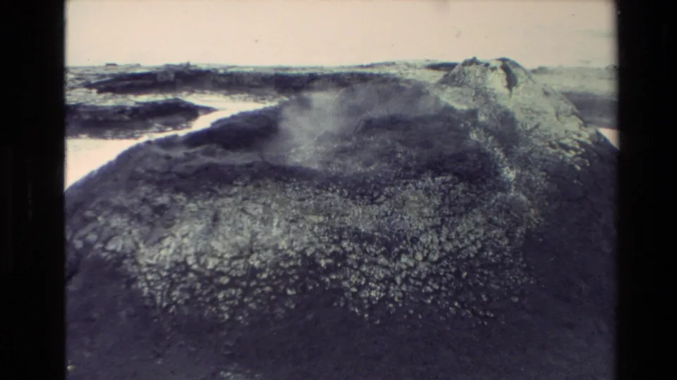1981 New Zealand 8mm frame showing a steaming geothermal mound across dark, crusted ground with pale mineral deposits.