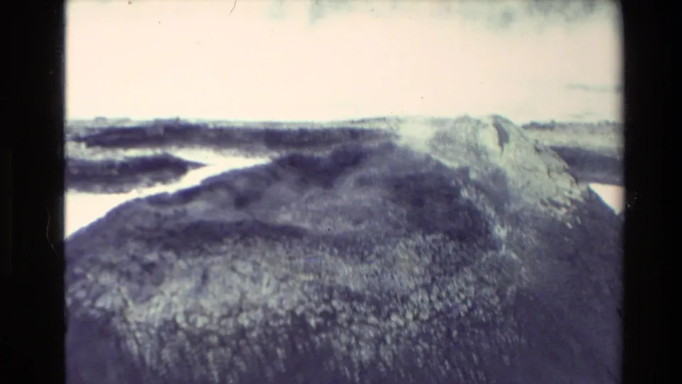 Vintage 8mm view of a New Zealand geothermal ridge with steam drifting over dark earth and pale mineral staining.