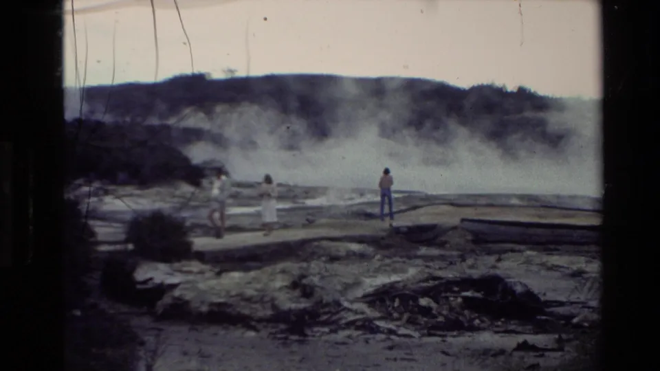 1981 New Zealand 8mm frame showing distant visitors watching steam vents across a rugged geothermal area.