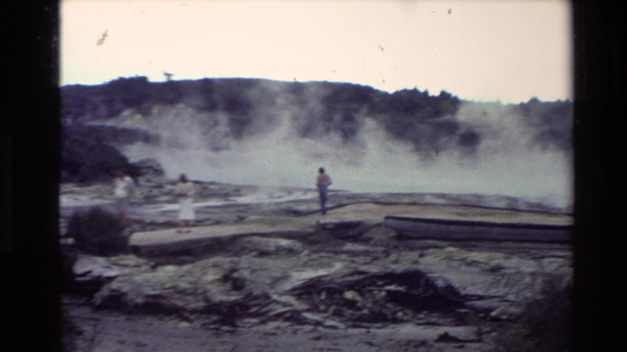 1981 New Zealand home-movie frame showing visitors near steam vents, pale mineral ground, low hills, and wooden boardwalks.
