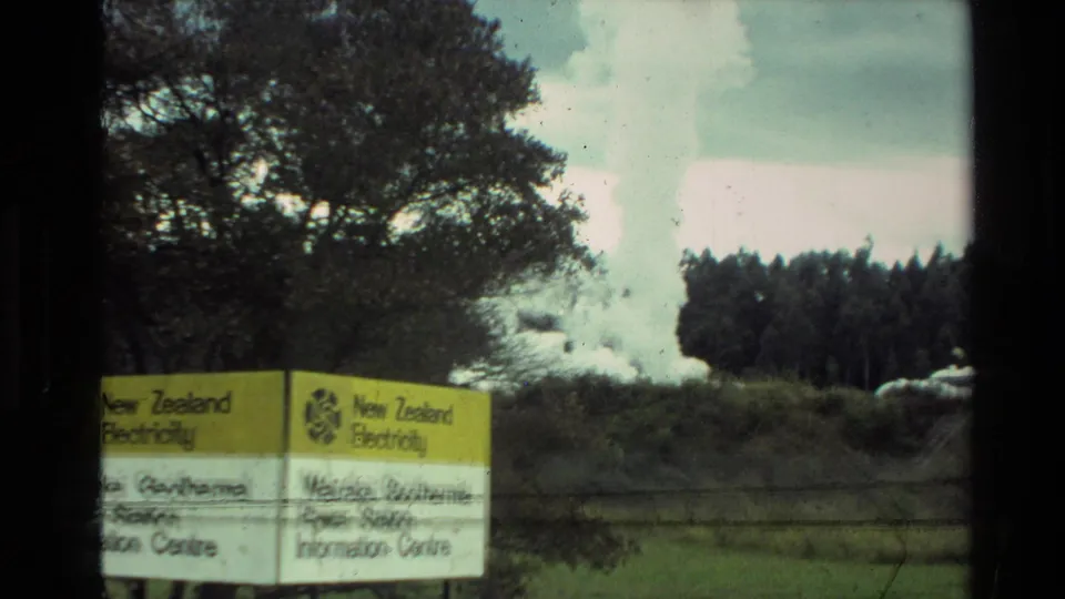 1981 New Zealand 8mm frame showing paired Wairakei geothermal signs, a fence, trees, grass, and steam rising in the distance.