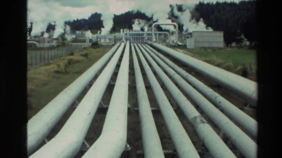 1981 New Zealand 8mm frame of large white geothermal pipes running toward industrial structures and visible steam at Wairakei.