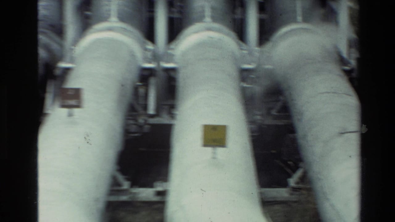 1981 New Zealand 8mm frame showing close-up insulated industrial pipes with small labels and soft handheld blur.