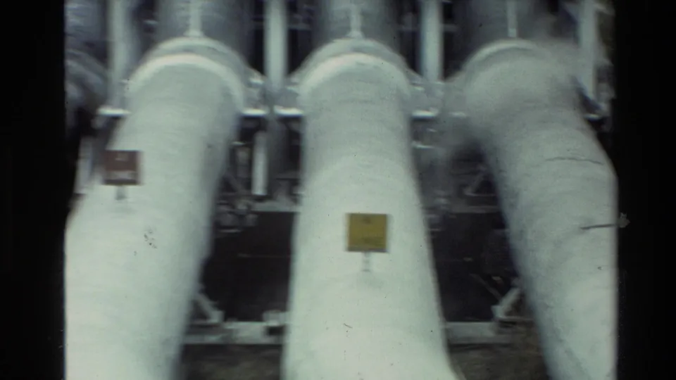 1981 New Zealand 8mm frame showing close-up insulated industrial pipes with small labels and soft handheld blur.