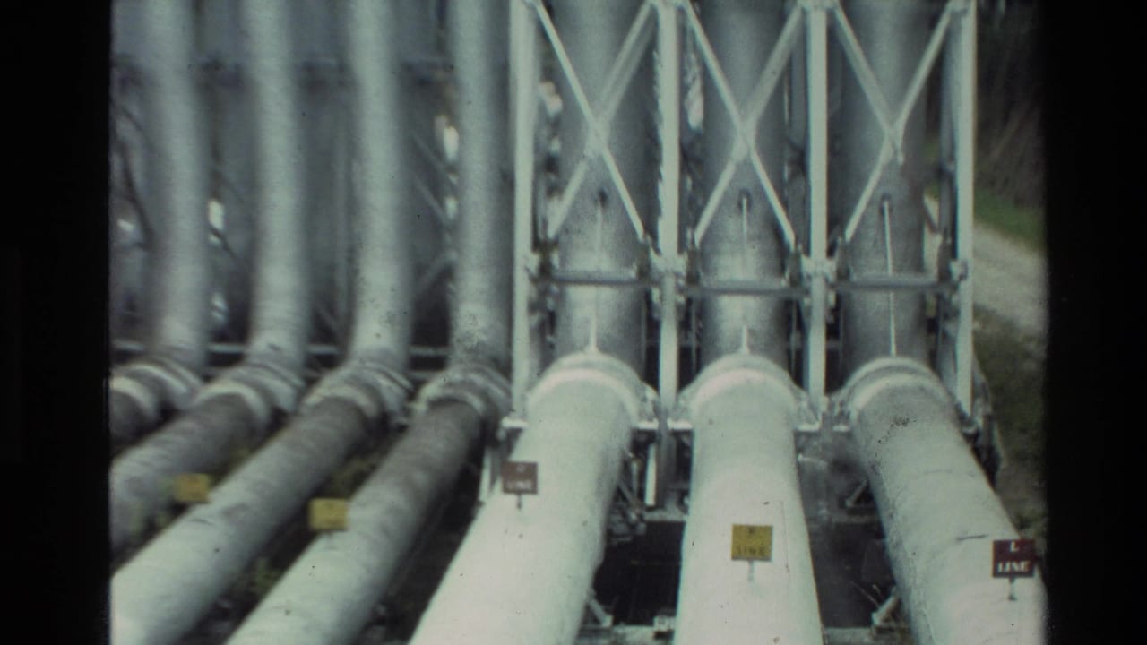 1981 New Zealand frame showing grey-white industrial pipes running through metal bracing with small visible line labels.
