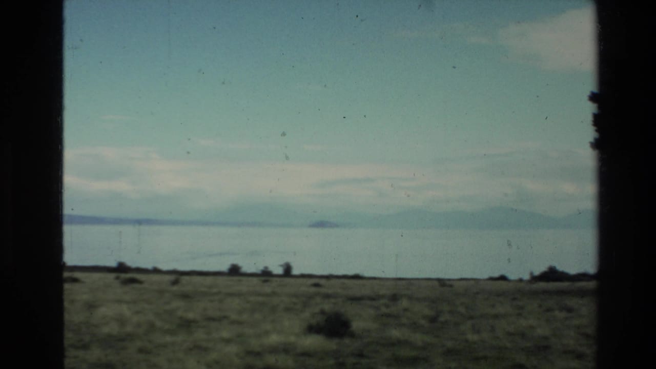 Open plain and water with distant hills framed by dark vertical window edges.