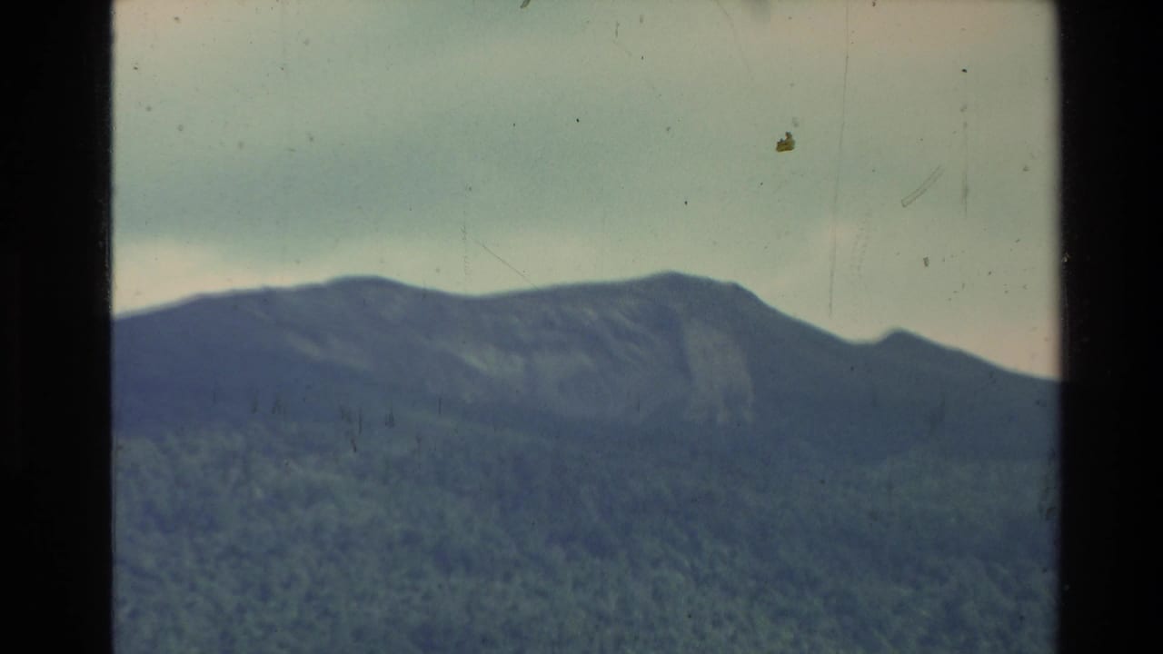 Soft 8mm view of a mountain ridge under cloudy sky, framed by dark film borders.