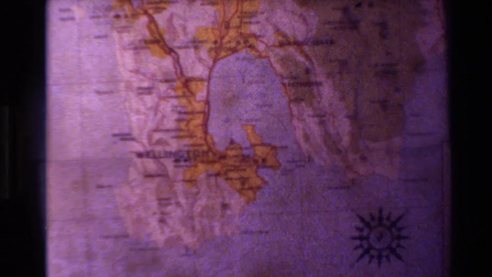 1981 New Zealand home-movie frame showing a close-up map detail with purple color cast, yellow land areas, and a compass rose.