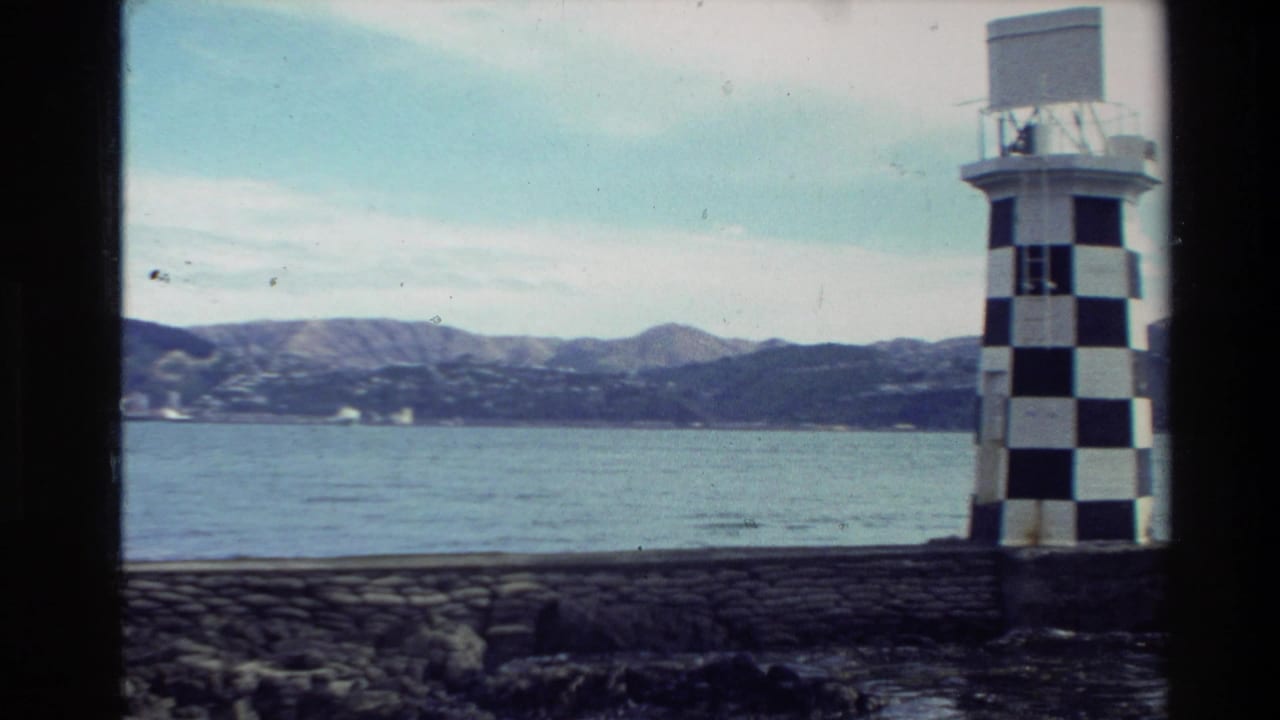 Black-and-white checked lighthouse-like structure beside harbor water with hills in the distance.