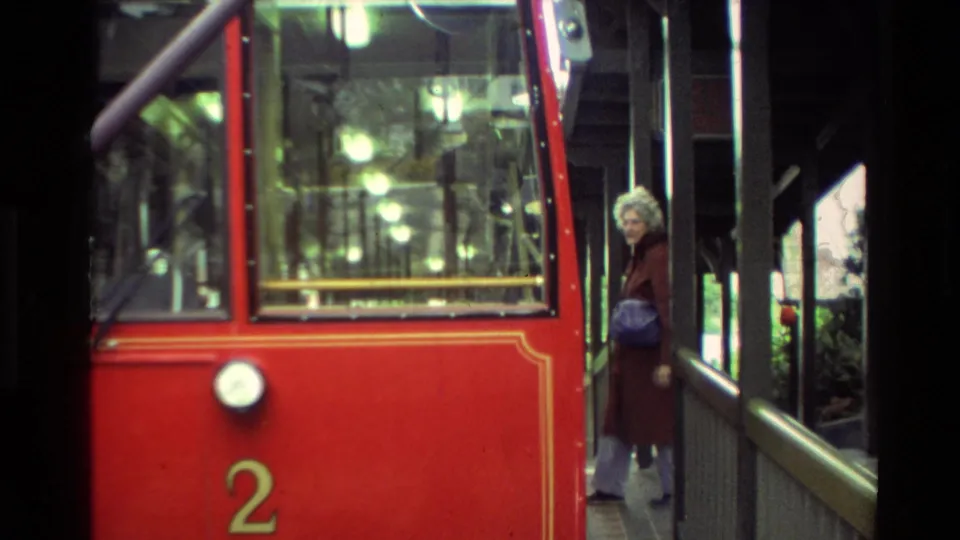 Close view of a red trolley or cable car marked 2, with a woman near the doorway and interior lights visible through the windows.