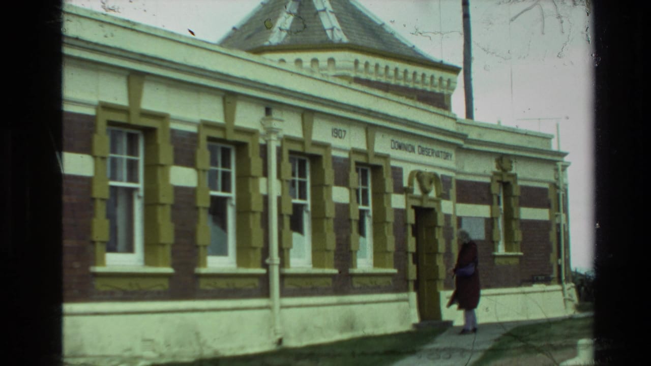 1981 New Zealand 8mm frame of the observatory entrance, showing windows, signage, and a visitor standing on the walkway.
