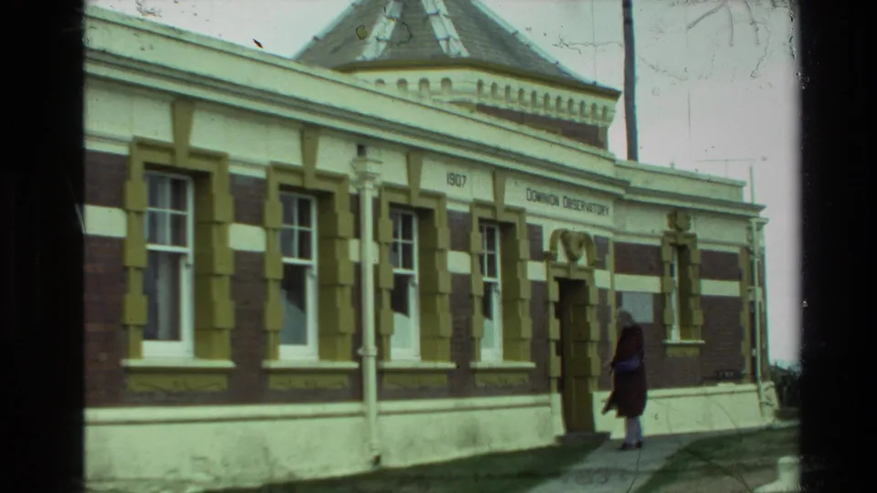 1981 New Zealand 8mm frame of the observatory entrance, showing windows, signage, and a visitor standing on the walkway.