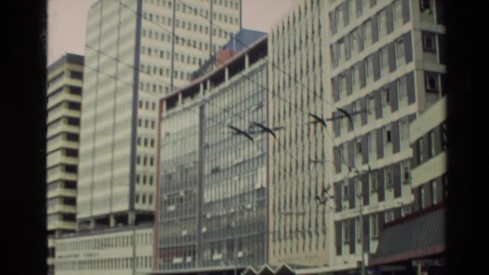 Close 1981 New Zealand downtown view showing office facades, overhead street wires, a streetlight, and lower commercial frontage.