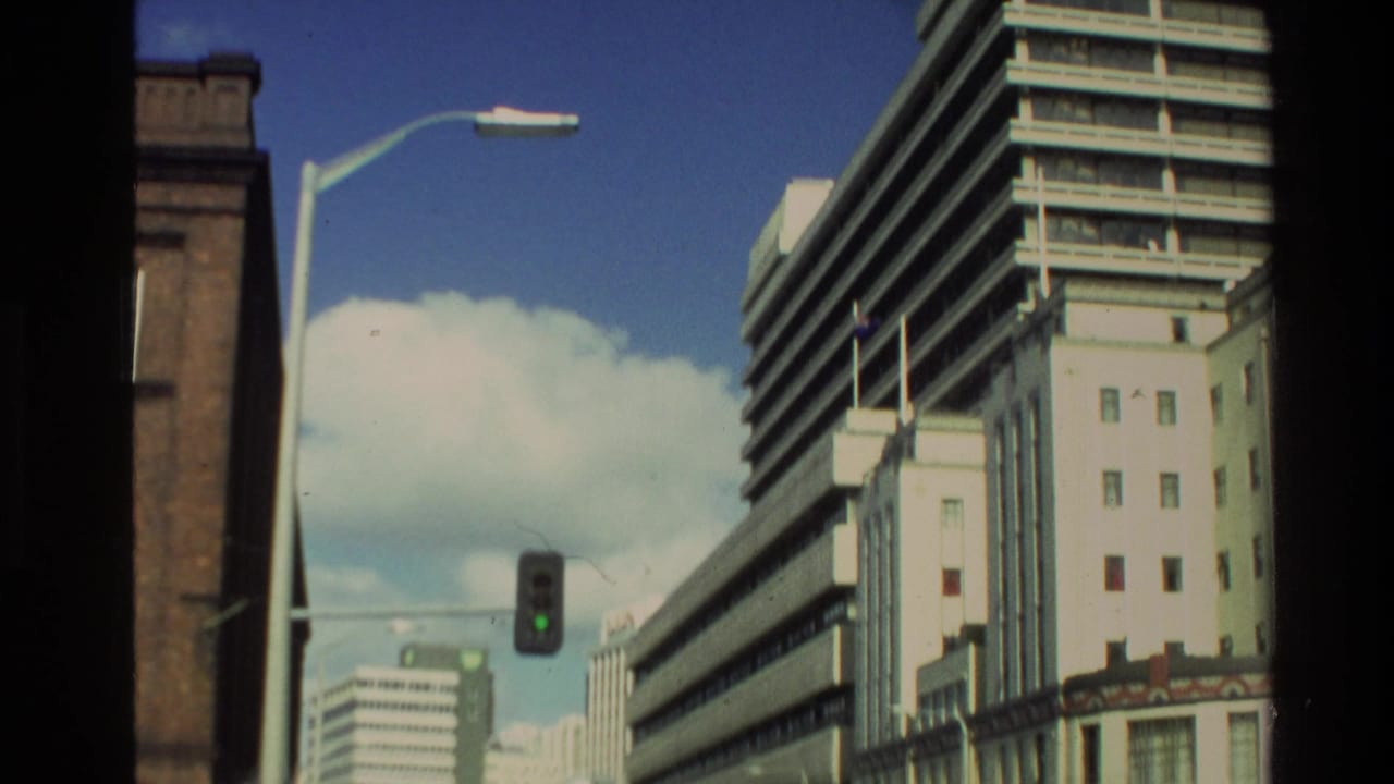 City street view with tall buildings, a green traffic light, cars, and blue sky.