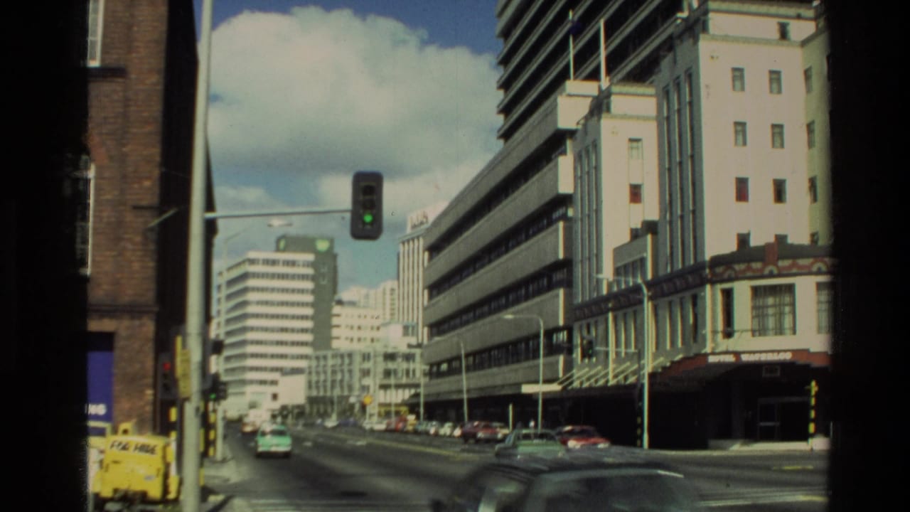 Urban street with office buildings, cars, a green traffic light, and storefront signs.