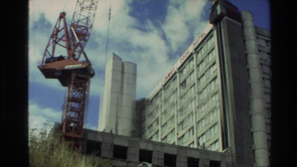 1981 New Zealand 8mm frame showing a construction crane next to a multi-storey city building and blue sky.