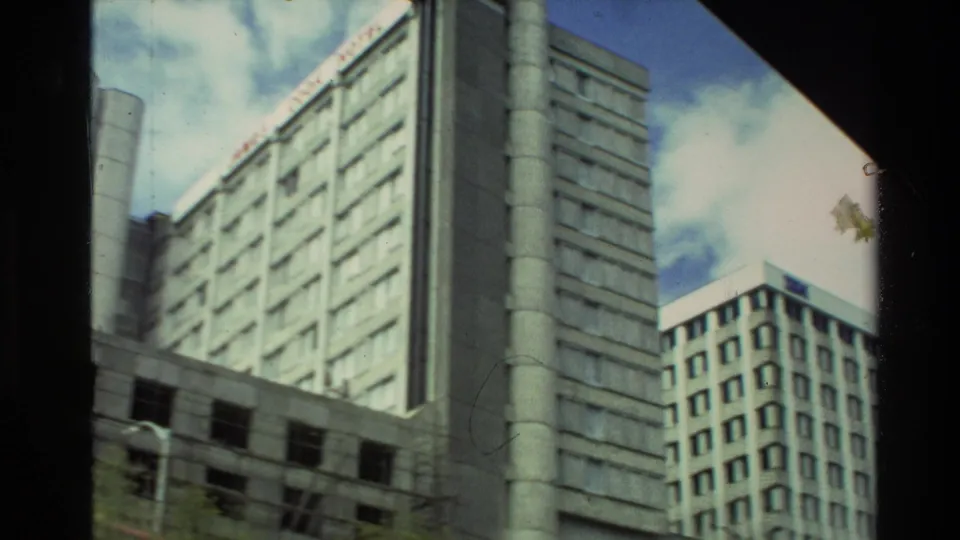 1981 New Zealand frame with tall urban buildings, a foreground structure, blue sky, and visible film gate edge.