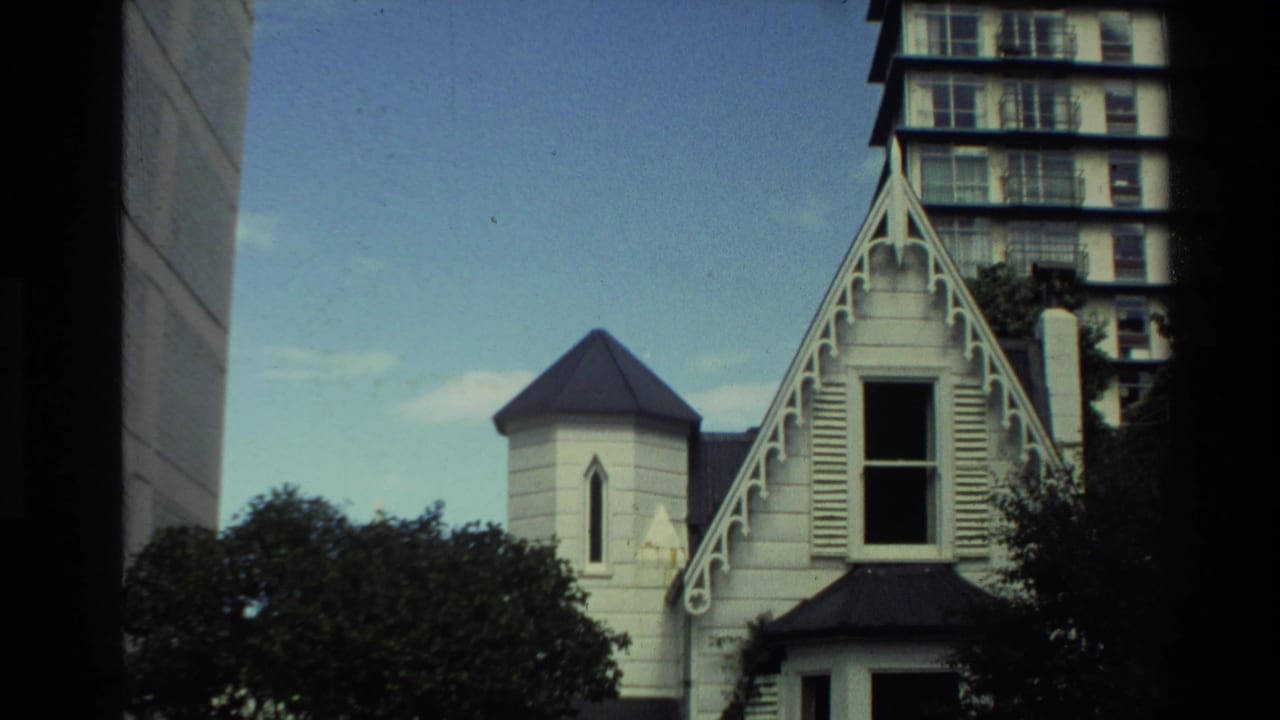 The camera frames the house's gable, turret, dark roofline, trees, and high-rise apartments in the supplied New Zealand 1981 clip.