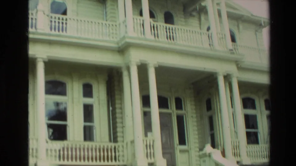 Closer view of the white Victorian-style porch, showing tall columns, balcony railings, arched upper windows, entry doors, and stair details.