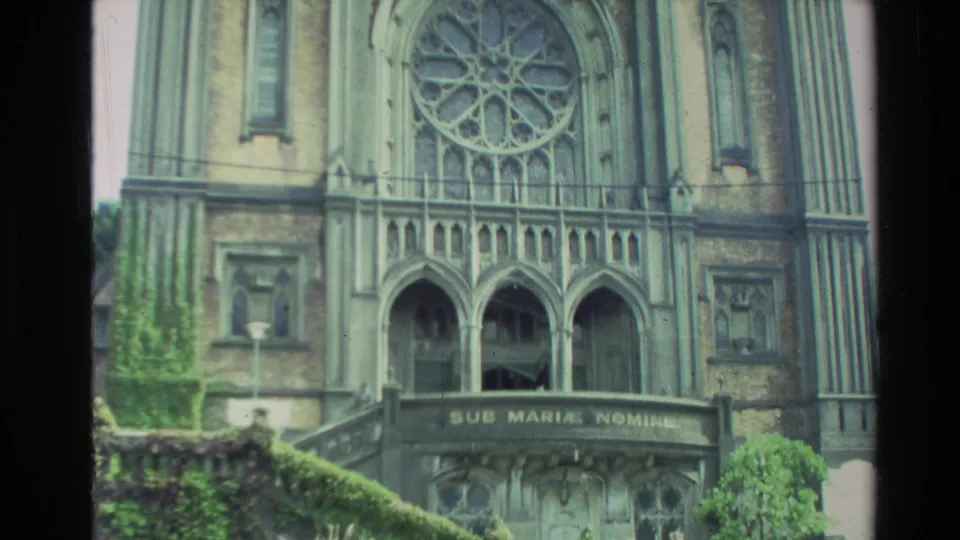 1981 New Zealand home-movie frame of a Gothic-style cathedral facade with a rose window, pointed arches, and front steps.