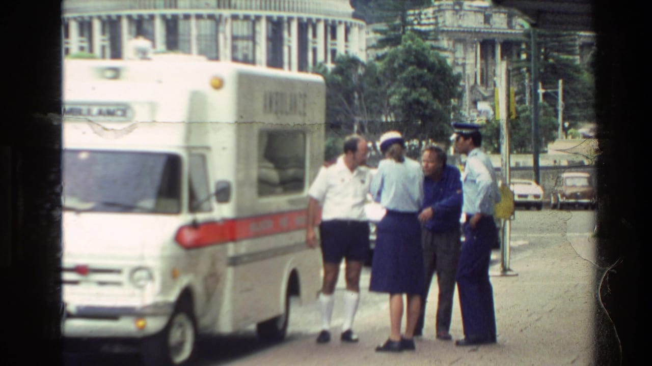 Uniformed people and a man stand beside a white ambulance on a city street.