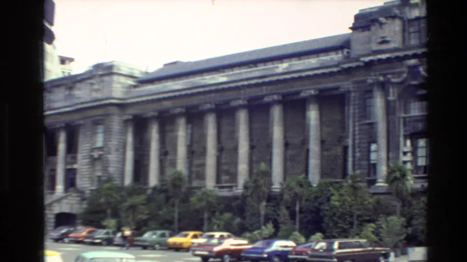 A Wellington street-side view shows a large columned building, trees, and parked cars in 1981 8mm footage.