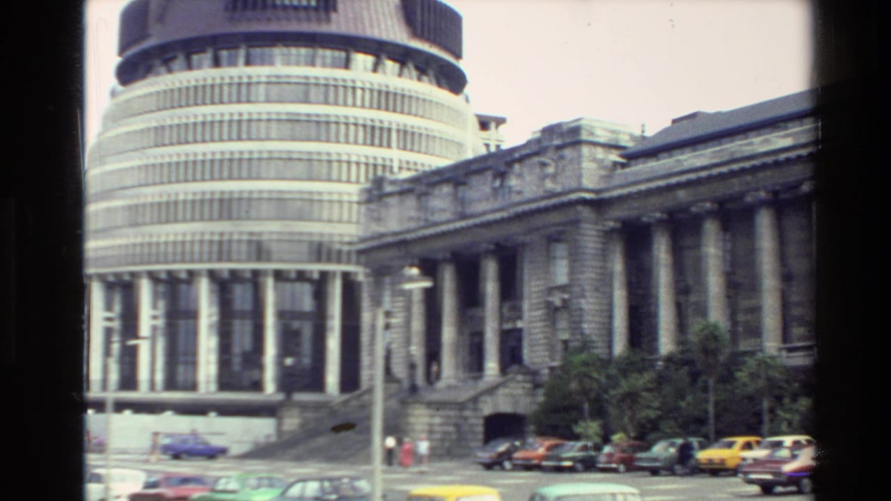 The Beehive and adjacent classical government building appear together above a street with 1980s cars and distant pedestrians.