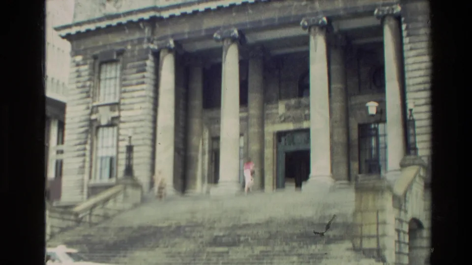 Closer 1981 New Zealand view of a classical government building entrance, showing tall columns, broad steps, and distant pedestrians.