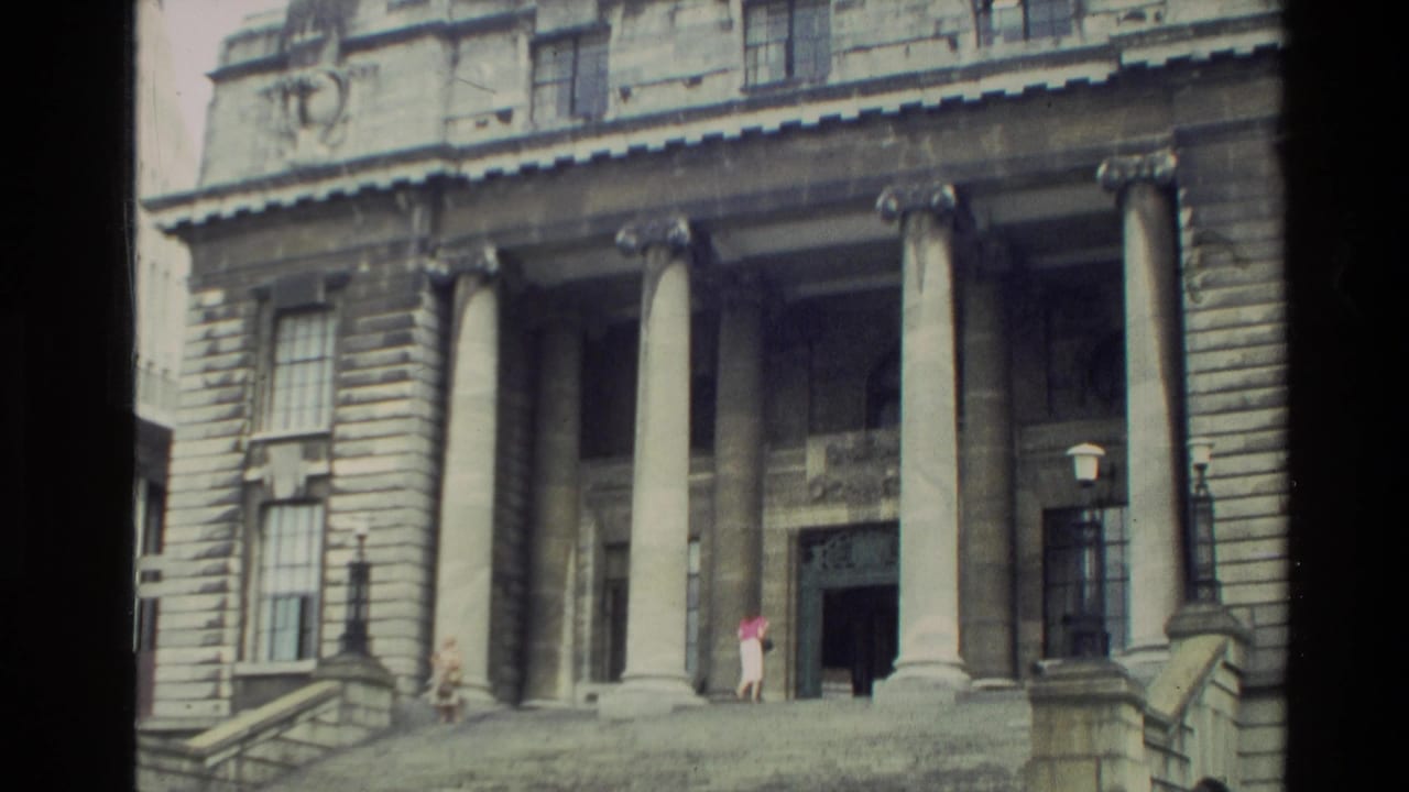 Stone building facade with tall columns, steps, and small figures near the entrance.