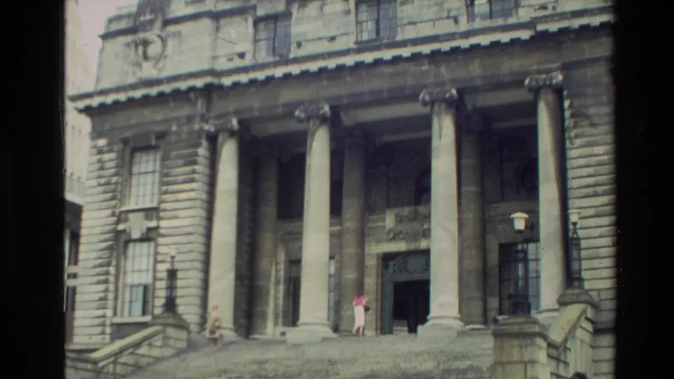 1981 New Zealand home-movie frame showing a grand stone public building with columns, steps, and people near the doorway.