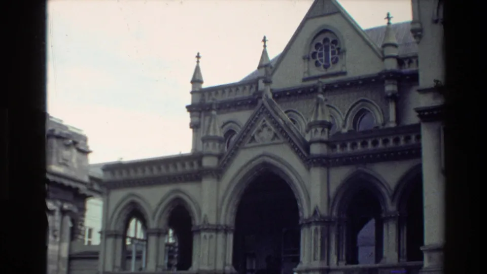 1981 New Zealand home-movie frame showing an ornate public building facade with pointed gables, arches, and decorative stonework.