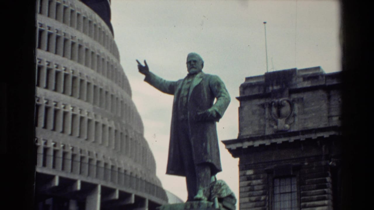 Full standing statue beside a curved modern building and older stone structure.