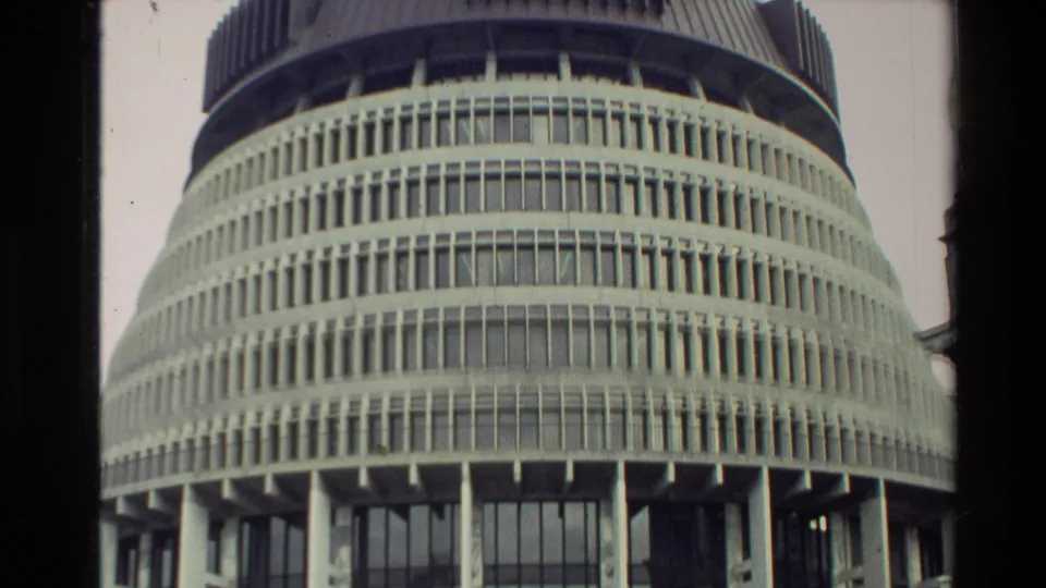 Low-angle 8mm view of the Beehive in New Zealand, with repeated concrete tiers, narrow window rows, tall columns, and soft film color.