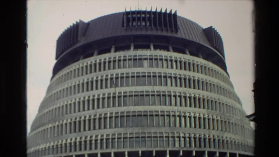 1981 home-movie frame of the Beehive’s rounded facade, showing stacked concrete bands, dense vertical glazing, roof detail, and edge vignetting.