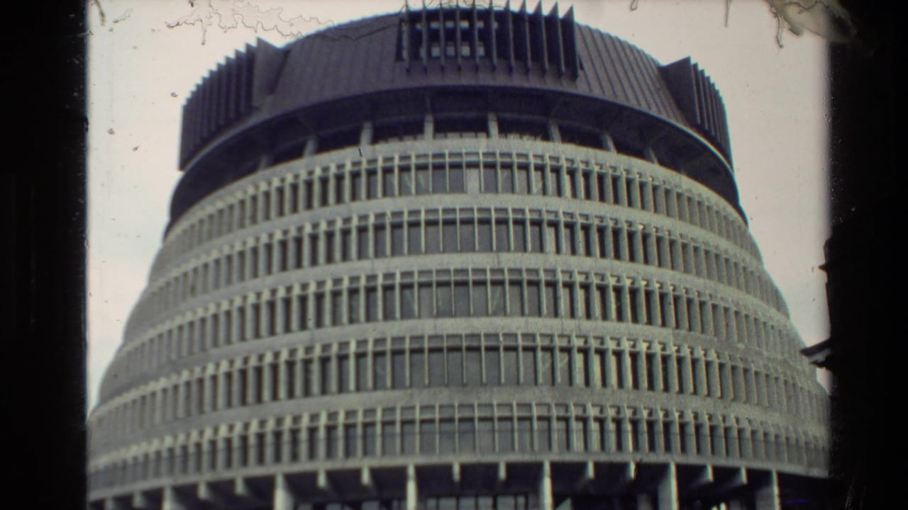 1981 New Zealand home-movie frame showing a cylindrical modernist building with stacked horizontal bands, vertical ribs, and a dark spiked upper section.