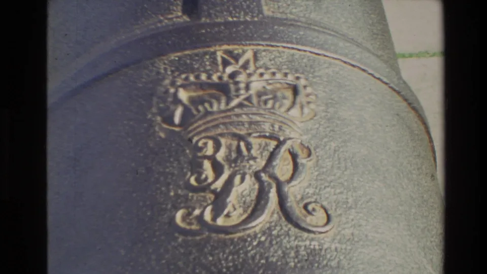 Close 8mm view of a raised royal-style crown and monogram cast into the metal surface of the cannon.